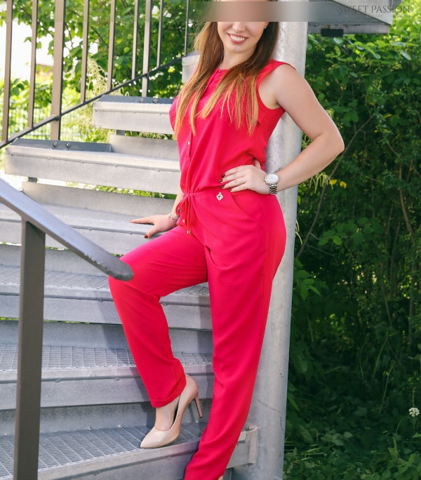 Sophia- VIP Escortmodel Berlin auf der Terasse im leuchtenden roten Jumpsuit.
