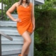 Liana -Escortdame Köln im orangenen Kleid in einem Garten stehend.