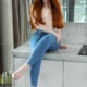 Amalia - Junge Escortdame Frankfurt in einer Jeans mit beigen High Heels auf einer Kommode sitzend.