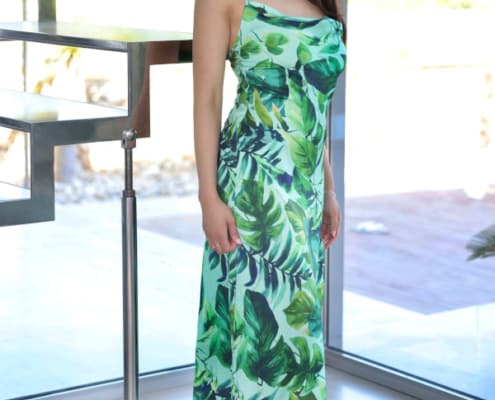 Alexandra - Elite Escort Frankfurt im langen grünen Sommerkleid mit High Heels vor einer Glastreppe stehend.