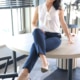 Luisa - Escort Remscheid in einer Bluse und Jeanshose mit High Heels auf einem Tisch sitzend.