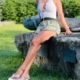 Joanna - Escort München im sommerlichen Outfit mit Rock und Top auf einer Wiese sitzend.