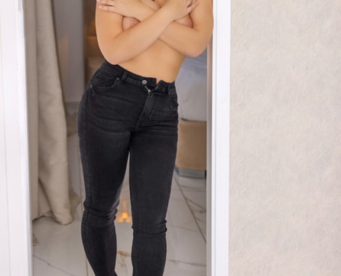 Johanna - Escortmodel Osnabrück in einer dunklen Jeans in einem Türrahmen stehend.
