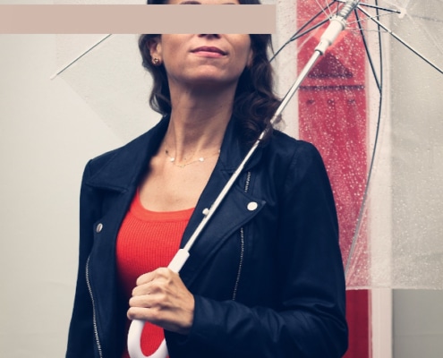 Gina - Escortmodel Köln mit Rock und Lederjacke unter einem Regenschirm stehend.