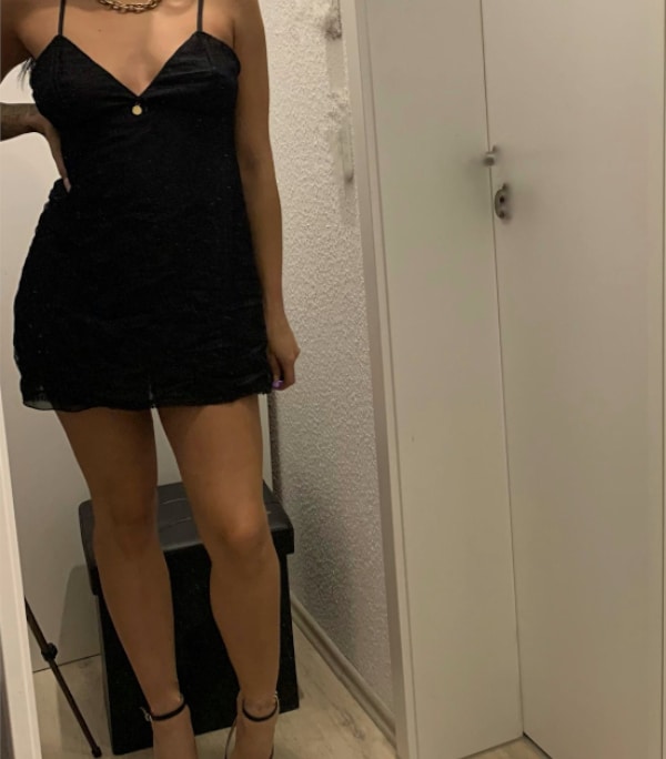Alessia - Escort Heilbronn in einem kurzen schwarzen Kleid vor einem Spiegel stehend.