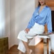 Luisa - Escort Bamberg in blauer Bluse und weissem Top seitlich auf einem Tisch sitzend.