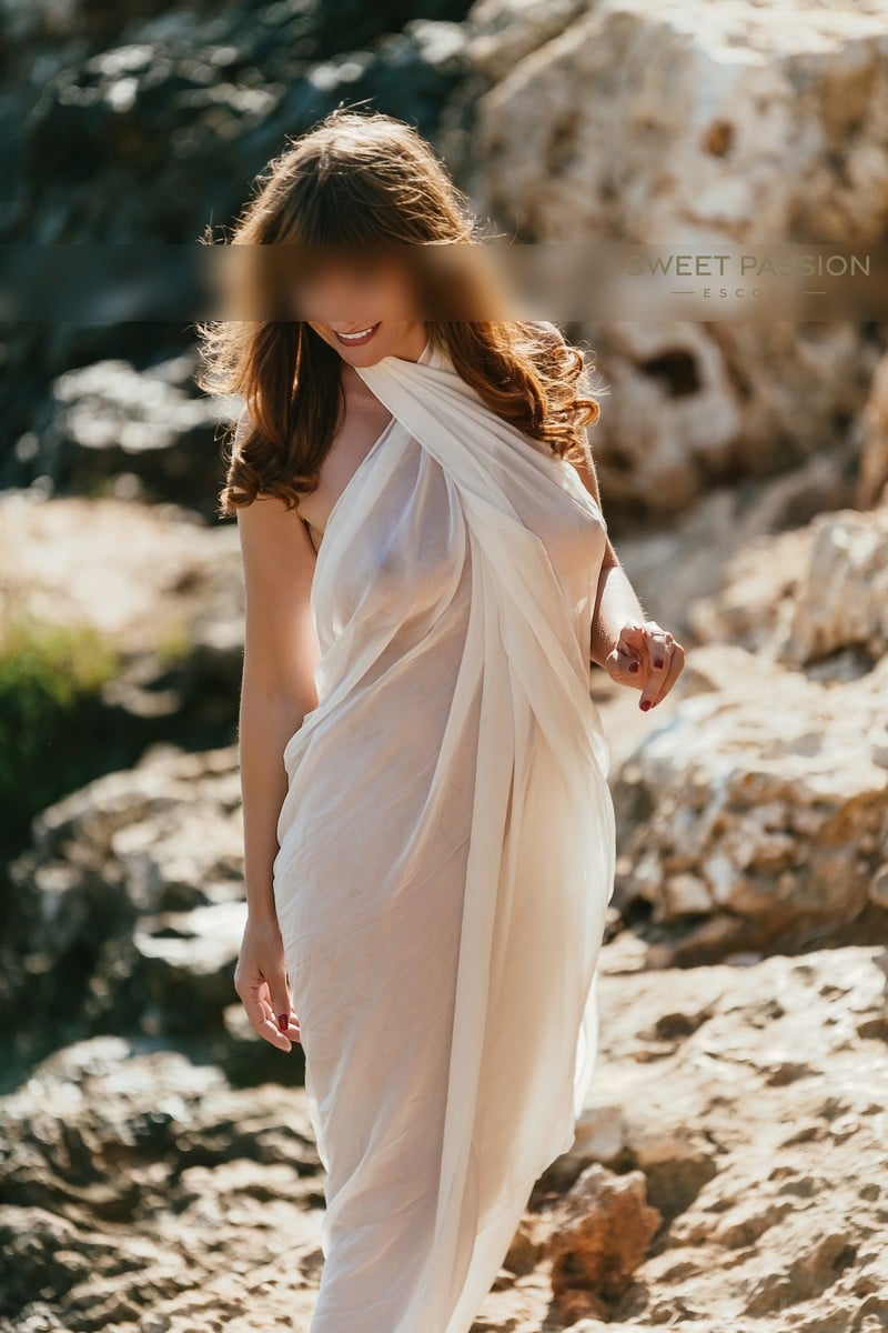 Evoto fabienne escort frankfurt zeigt sich seitlich stehend in einem weißen langen kleid, ihre langen braunen haare sind offen und lockig, sie zeigt ihr wunderschönes lächeln, reifes escort frankfurt