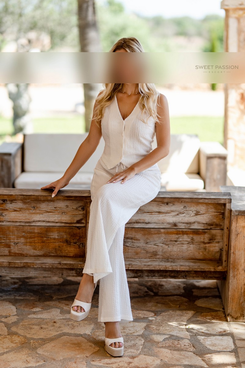 isabella – schlankes escort duesseldorf isabella - schlankes escort duesseldorf sitzt im weisses Kostüm und Highheels auf der Terasse. Ihre Beine sind überkreuzt und ihre blonden Haare fallen über ihre Schultern.